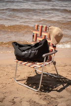Beach chair with a patterned backrest and 'lake it easy' bag on a sandy beach.